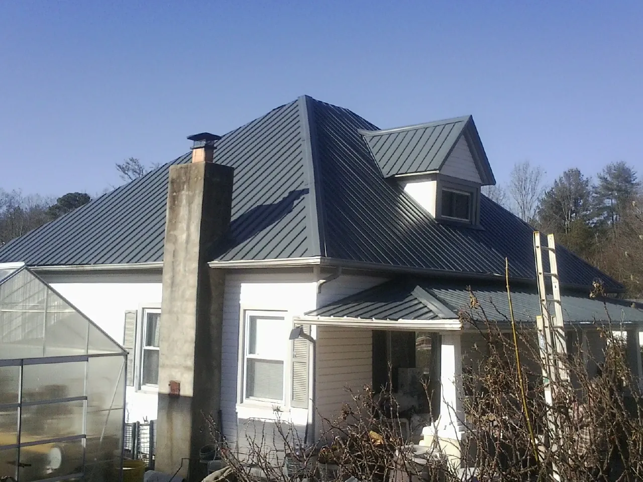 Dark blue standing seam metal roof on a white farmhouse with dormer — Slate & Tile Roof Repair by Roofing Brothers in Drummond