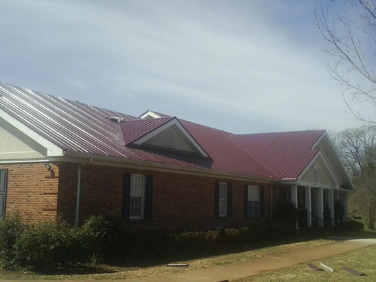 Red metal roof with gabled entries on a long brick building, from a Hail Damage Roof Repair job in Drummond