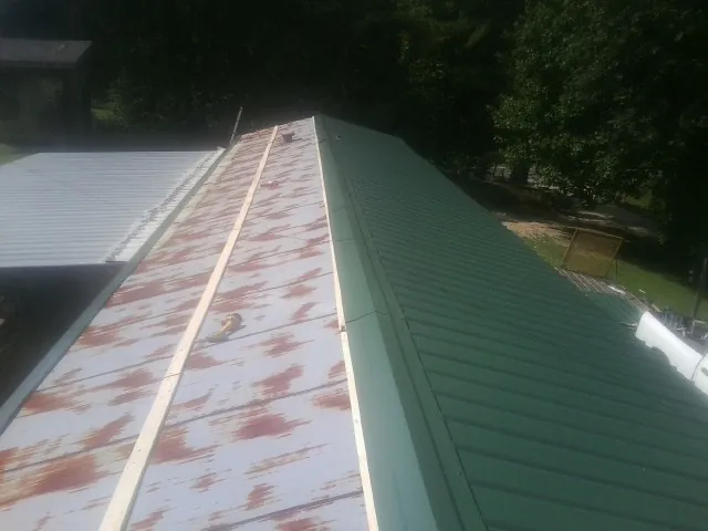 Old rusted panels beside newly installed green metal roofing — Wind Damage Roof Repair by Roofing Brothers in Drummond