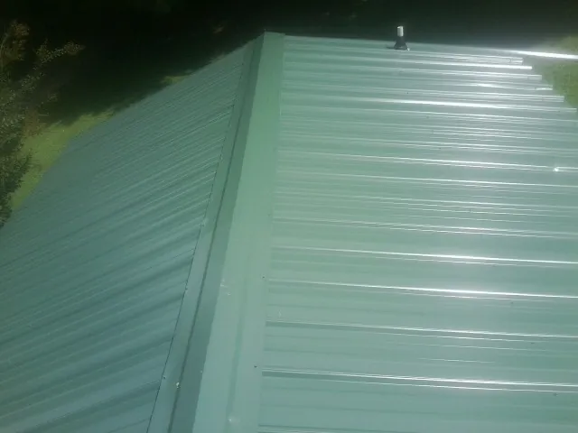 New green metal panels meeting at the ridge of a roof — Flat Roof Repair work by our crew in Drummond