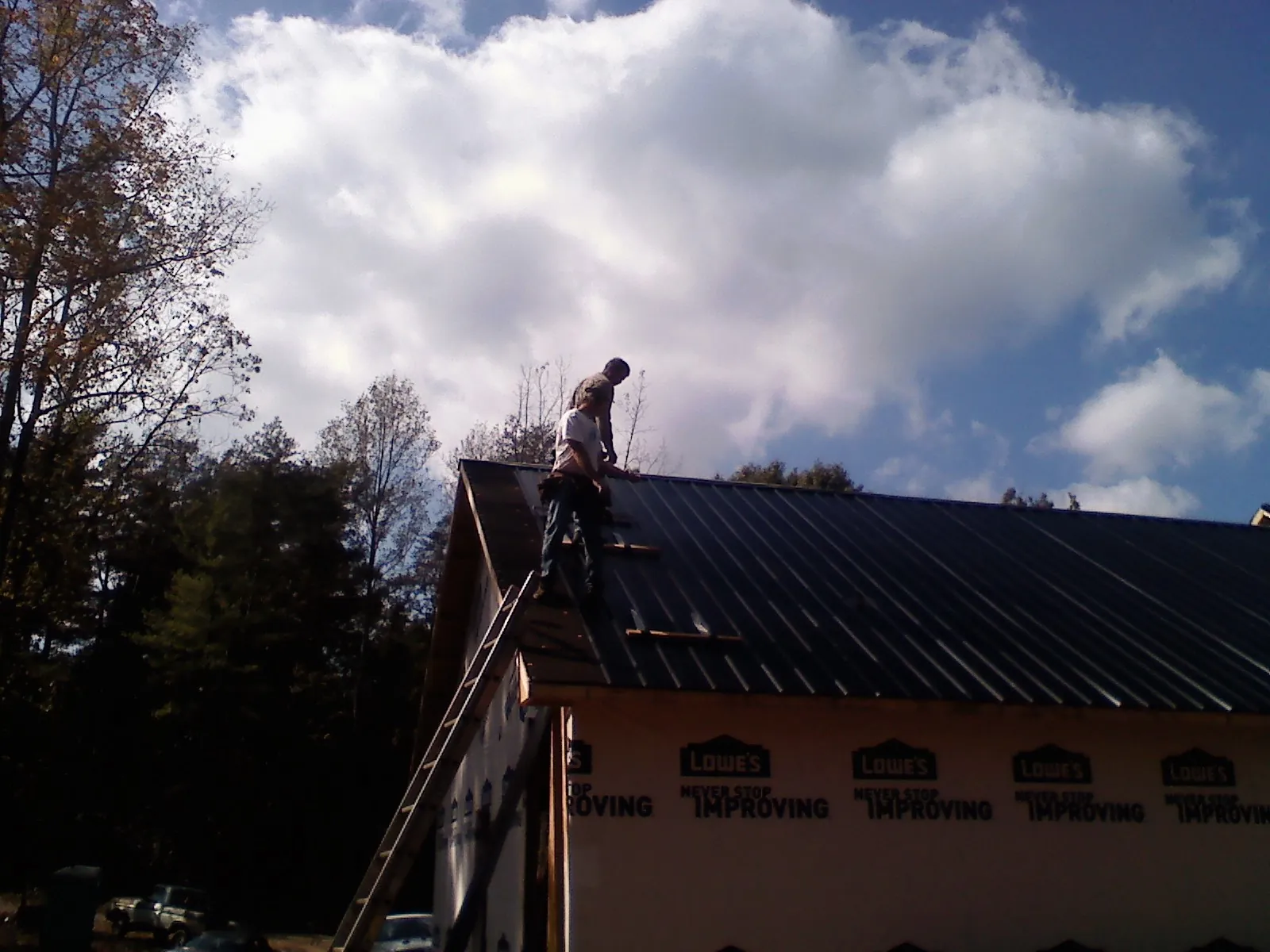 Roofer fastening dark metal panels high against a cloudy sky, from a Roof Inspection job in Drummond